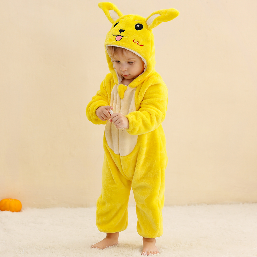 Et billede af et nuttet og blødt gult Pikachu-kostume til børn, formet som en heldragt i fleece. Dragten har en hætte med Pikachus ansigt og de karakteristiske lange ører med sorte spidser, samt to brune striber på ryggen og en lynlås foran.
