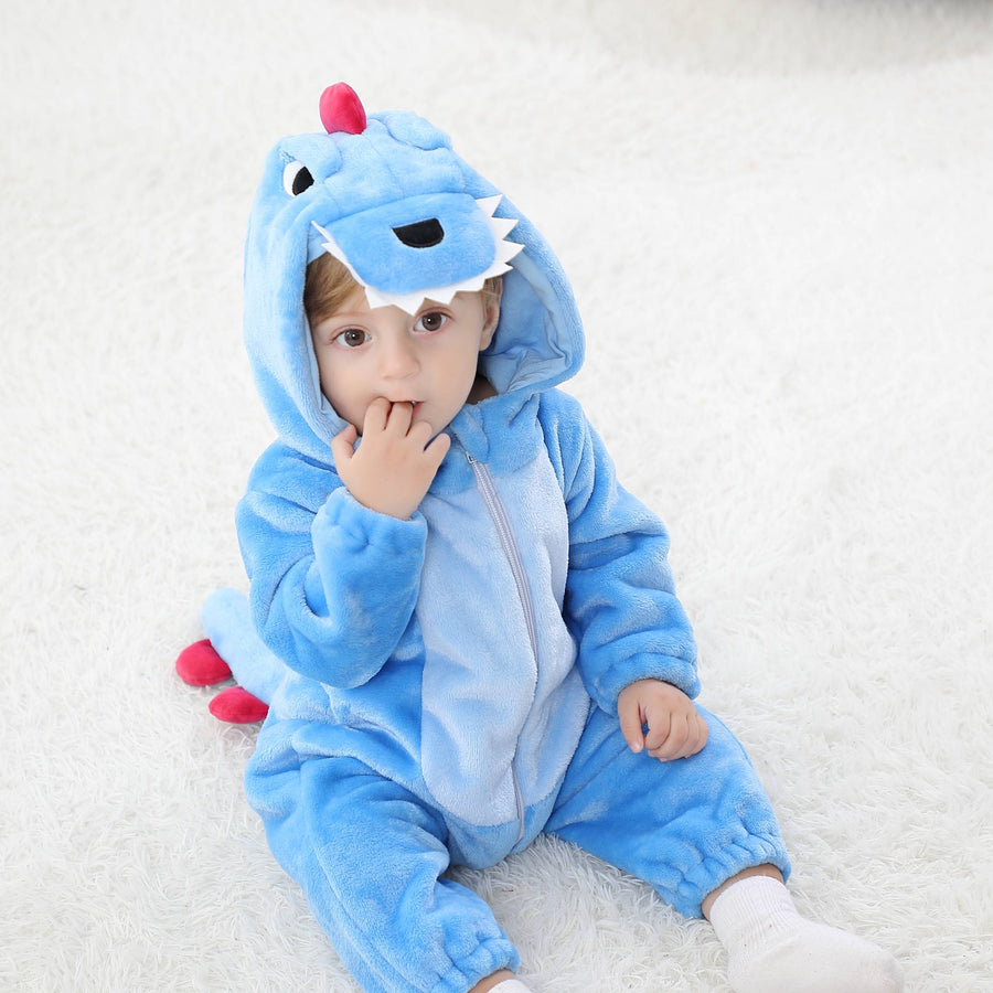 Dette billede viser et nuttet og blødt blåt dinosaur-kostume til børn, formet som en heldragt i behageligt flannel. Dragten har en hvid mave, en række mørkeblå takker ned langs ryggen og en matchende hætte med et sødt dino-ansigt, der gør den ideel til leg og fastelavn.