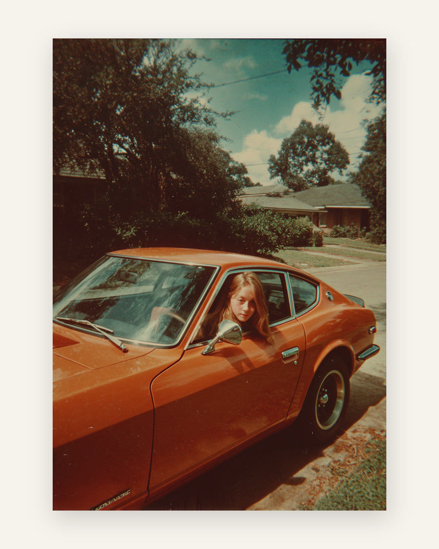 Nostalgisk retro-foto af en ung kvinde i vinduet af en brændt-orange klassisk sportsvogn en solrig sommerdag