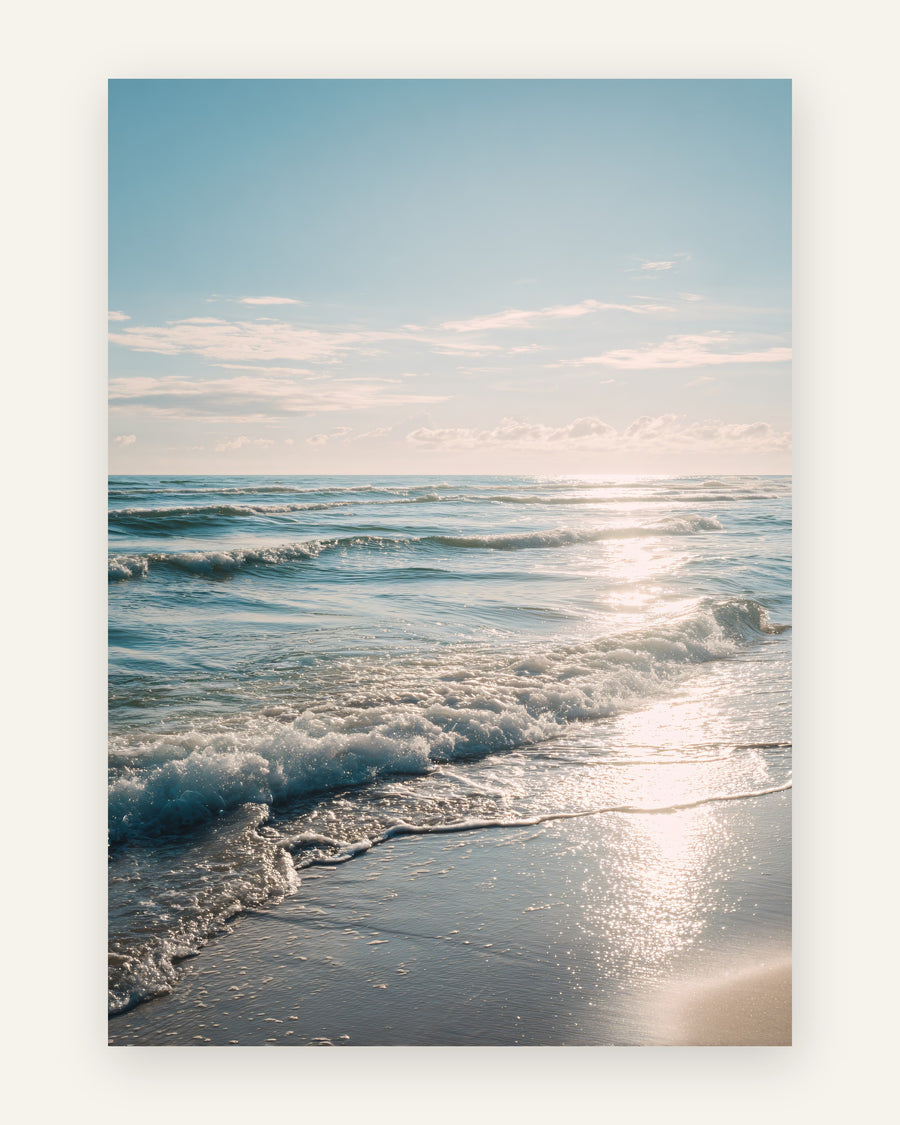Plakat med en solbeskinnet strand, hvor bløde bølger ruller ind mod kysten under en lyseblå himmel med glitrende refleksioner, i fotostil