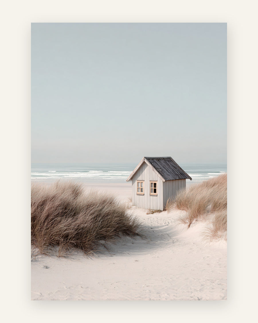 Fotografisk plakat med lille gråt strandhus i hvide klitter med klitgræs og roligt hav