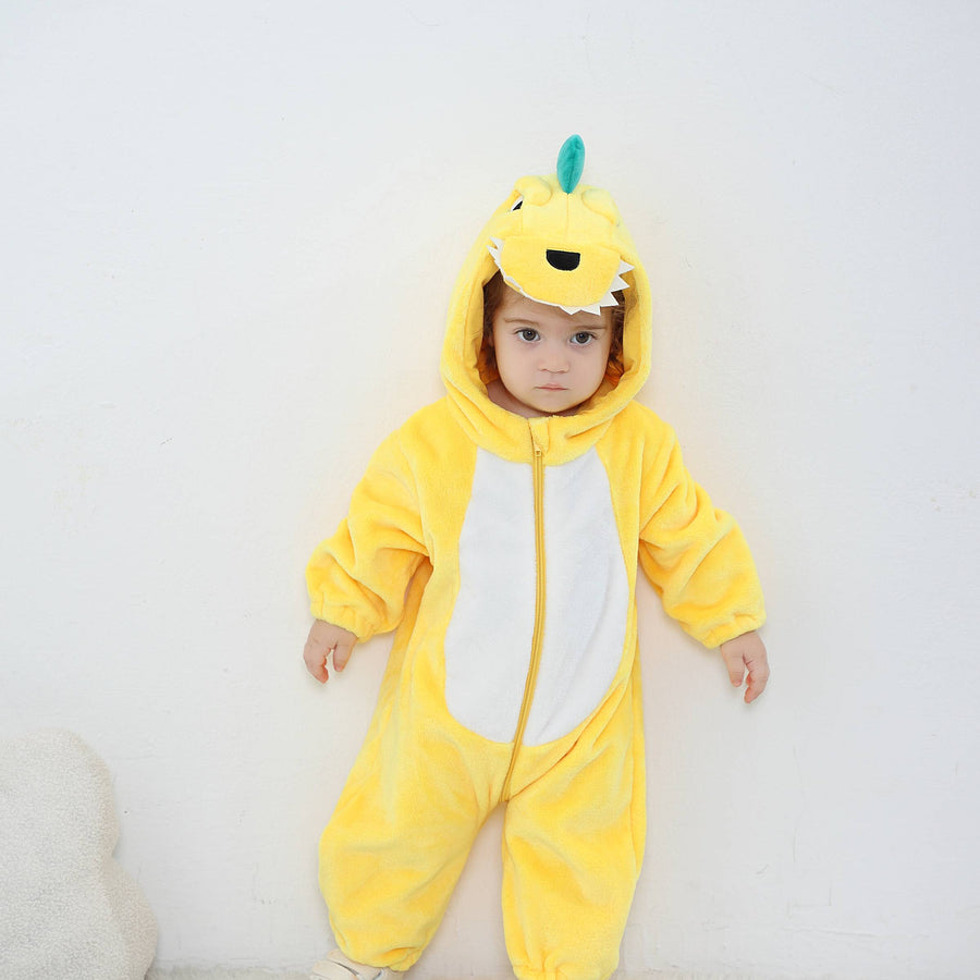 Et charmerende og blødt gult dinosaur-kostume til børn, formet som en heldragt i behageligt flannelmateriale. Dragten har en hvid mave, en række orange pigge ned langs ryggen og en sød hætte med store øjne og små tænder, der fuldender det legesyge look.