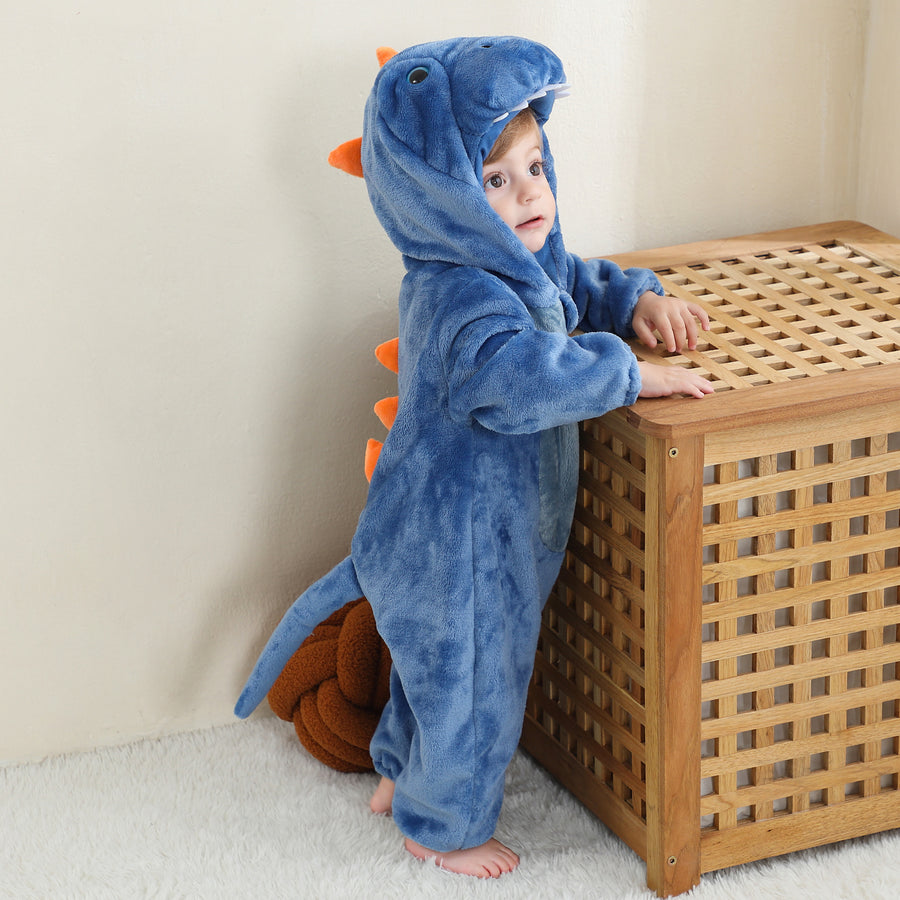 Et blødt og nuttet blåt T-Rex kostume til børn, formet som en behagelig heldragt med en lang hale, sjove pigge på ryggen og en hætte med et detaljeret dinosauransigt og hvide tænder.