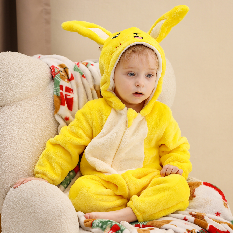 Et nuttet og blødt gult Pikachu-kostume til børn, formet som en heldragt i blødt stof. Dragten har en karakteristisk hætte med lange ører med sorte spidser, et broderet ansigt med røde kinder og en lynlås foran for nem påklædning.