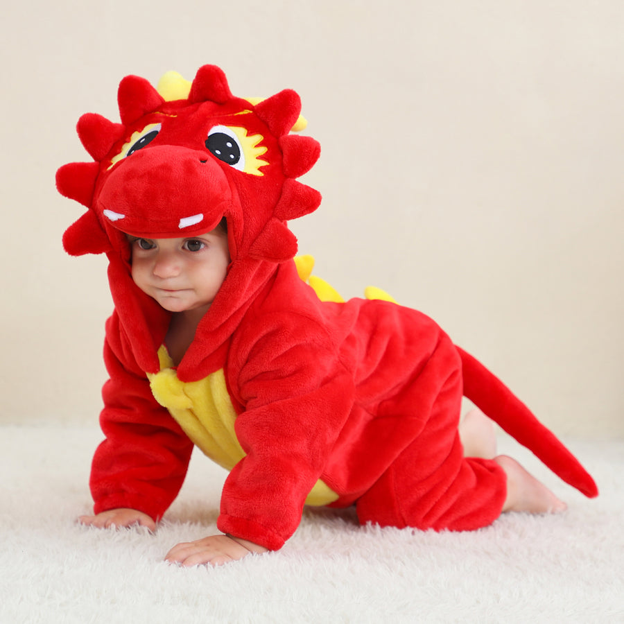 Dette billede viser et nuttet og blødt rødt dinosaurkostume til børn, lavet af behageligt flannelmateriale. Dragten har en lys mave, små takker langs ryggen og en sød hætte med ører, hvilket gør den perfekt til fastelavn eller kreativ leg.