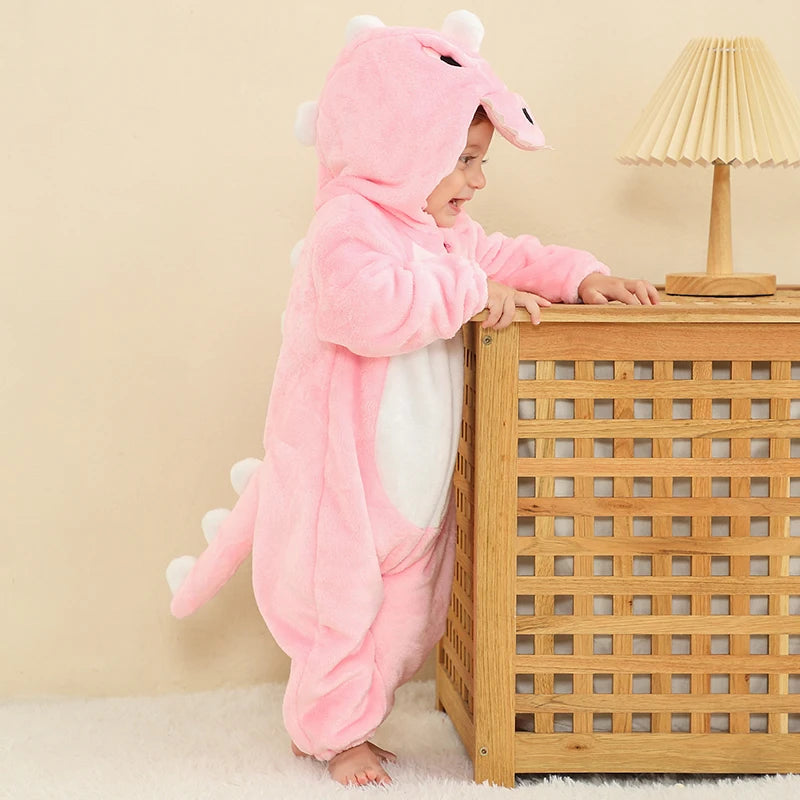 Dette billede viser et nuttet og blødt lyserødt T-Rex kostume til børn, fremstillet i behageligt flannelmateriale med et detaljeret skælmønster. Dragten har en fastgjort hætte med hvide tænder og øjne samt en polstret hale bagpå, hvilket gør den perfekt til både fastelavn og sjov leg.