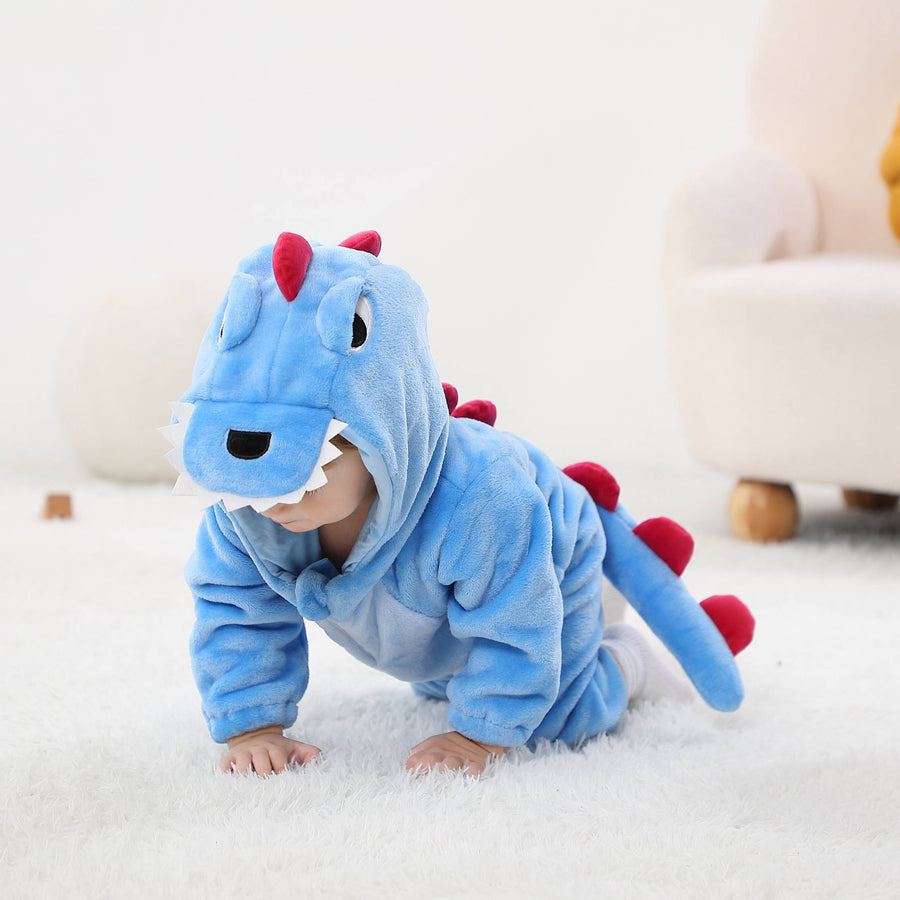 Billedet viser et nuttet og blødt blåt T-Rex kostume til børn, set fra siden for at fremhæve den lange hale med mørkeblå takker. Dragten er lavet af behageligt flannelmateriale med en hvid mave og en detaljeret hætte, der forestiller et dinosaurhoved med øjne og små tænder.
