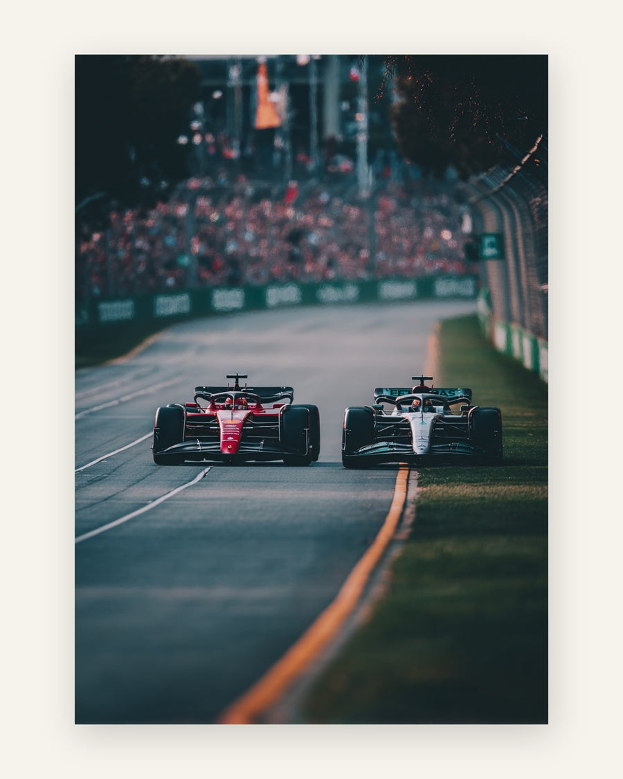 To Formel 1-racerbiler side om side set bagfra, en rød og en mørk bil foran fyldte tribuner