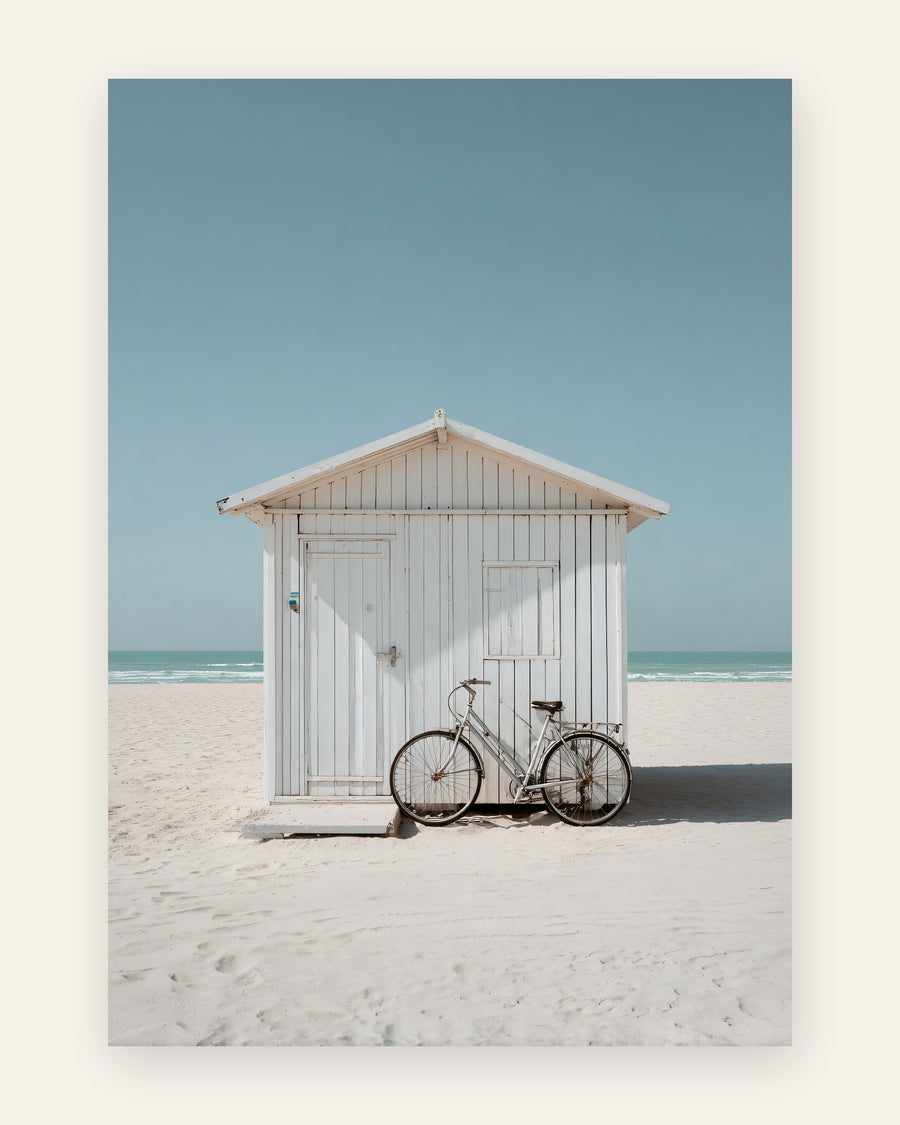 Fotografisk plakat med hvid træstrandhytte og vintage cykel på lys sandstrand med turkis hav og blå himmel