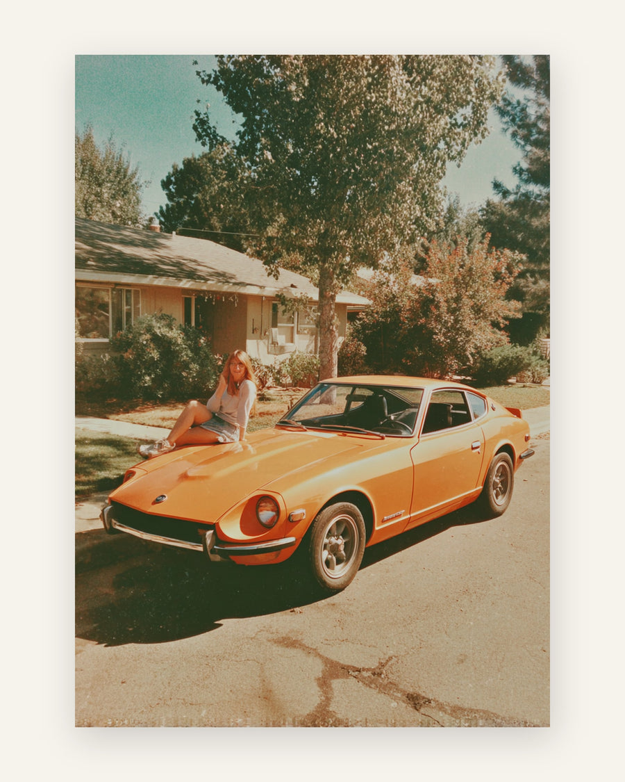 Nostalgisk retro-foto af en ung kvinde på kølerhjelmen af en klassisk orange sportsvogn i en solrig indkørsel