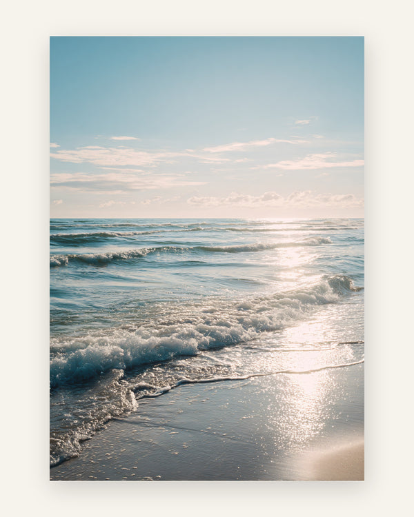 Plakat med en solbeskinnet strand, hvor bløde bølger ruller ind mod kysten under en lyseblå himmel med glitrende refleksioner, i fotostil